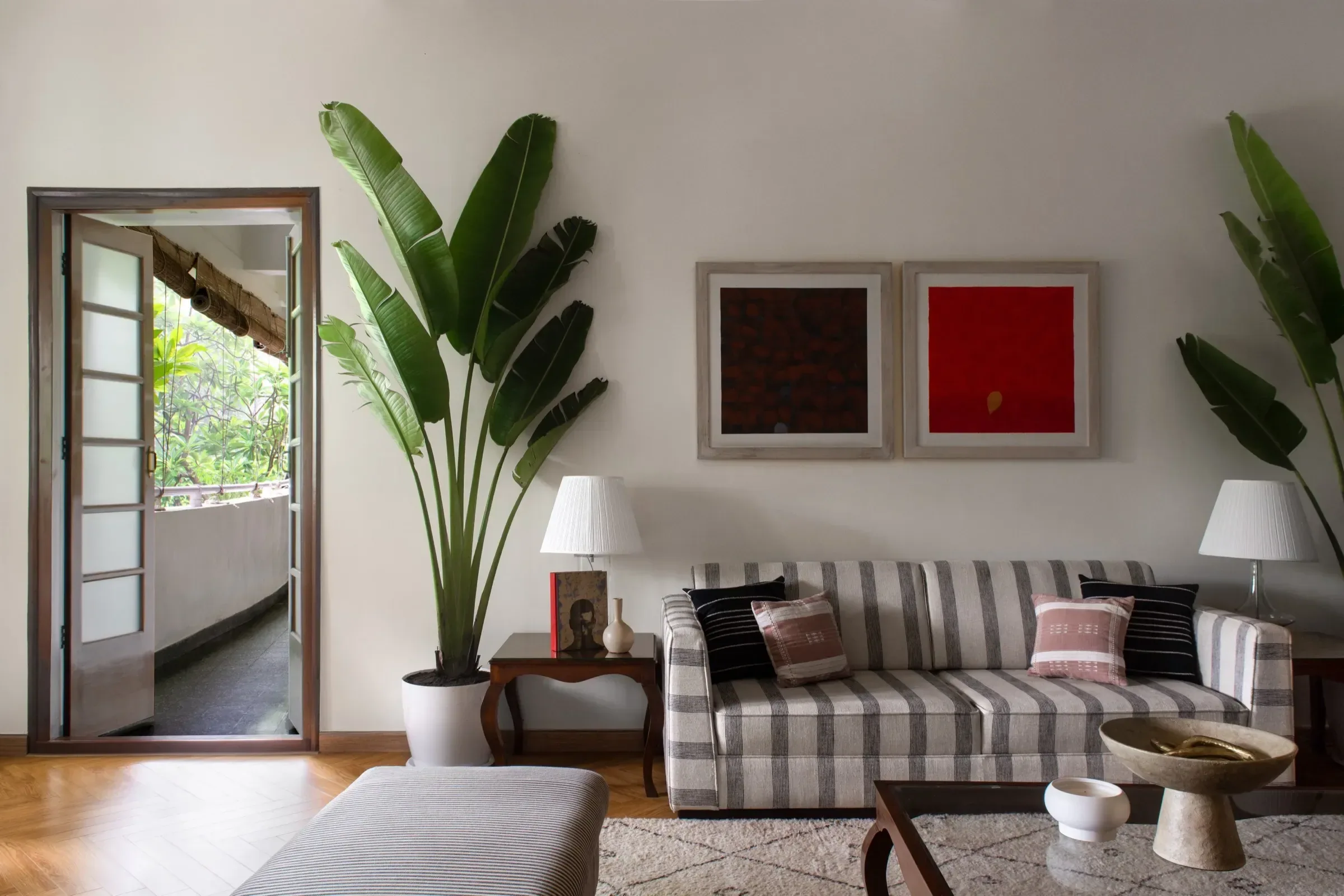Living room with striped sofa, banana plants and framed art by Sonia Gehlot