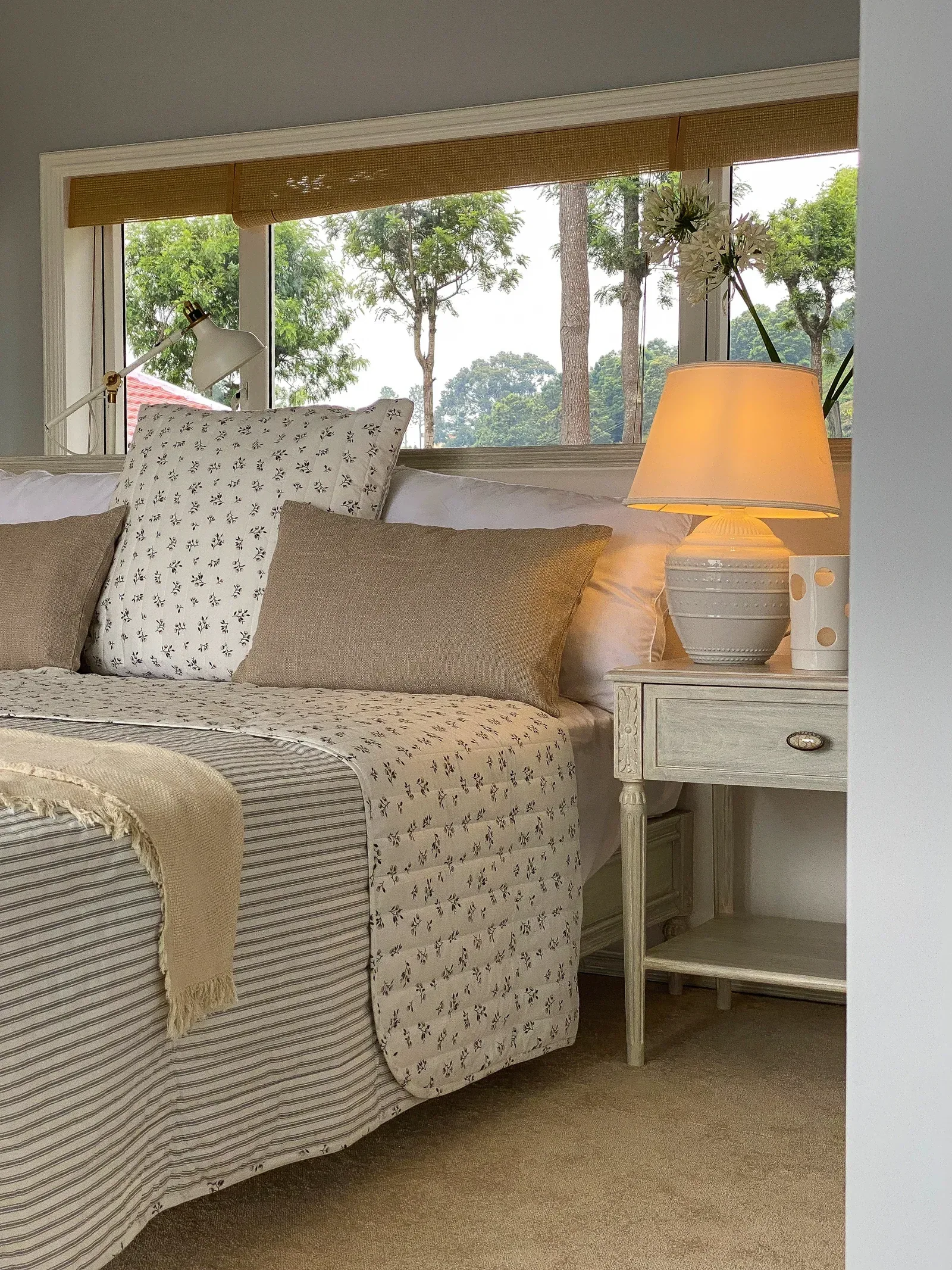 A dressed bed with a lamp and trees through the window at Coonoor by Sonia Gehlot