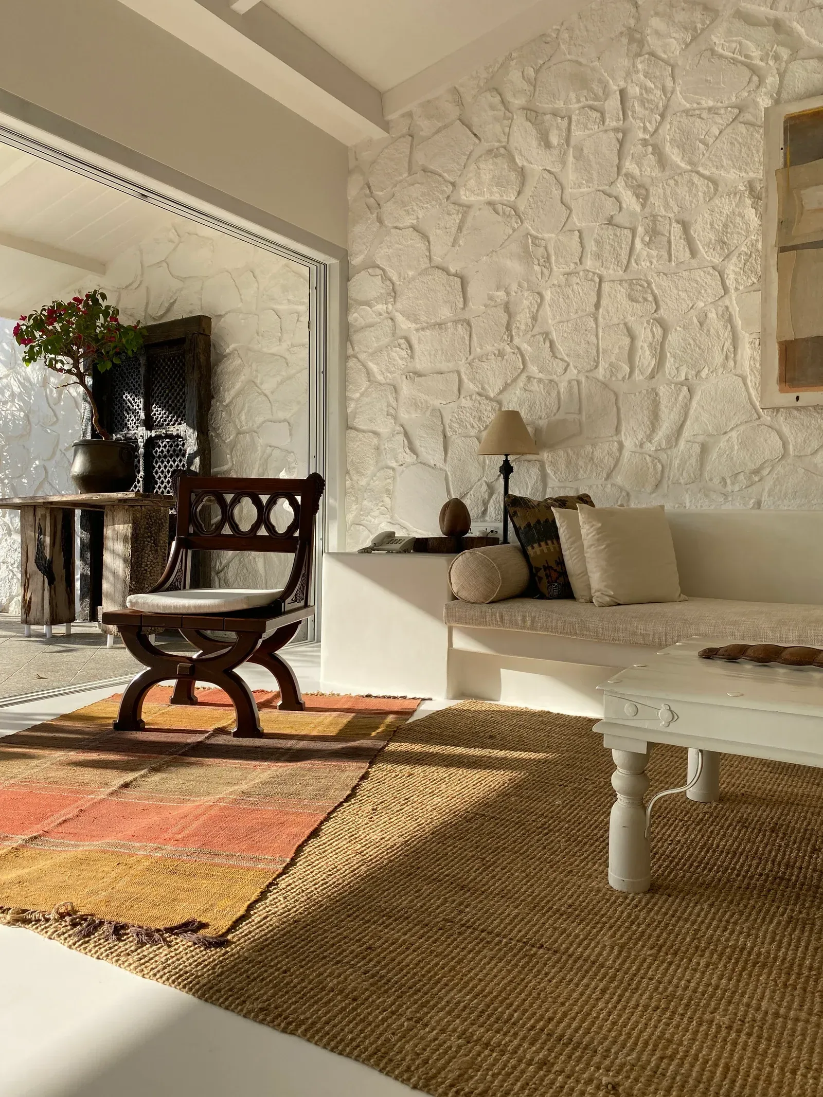 A carved timber chair against a textured white stone wall by Sonia Gehlot